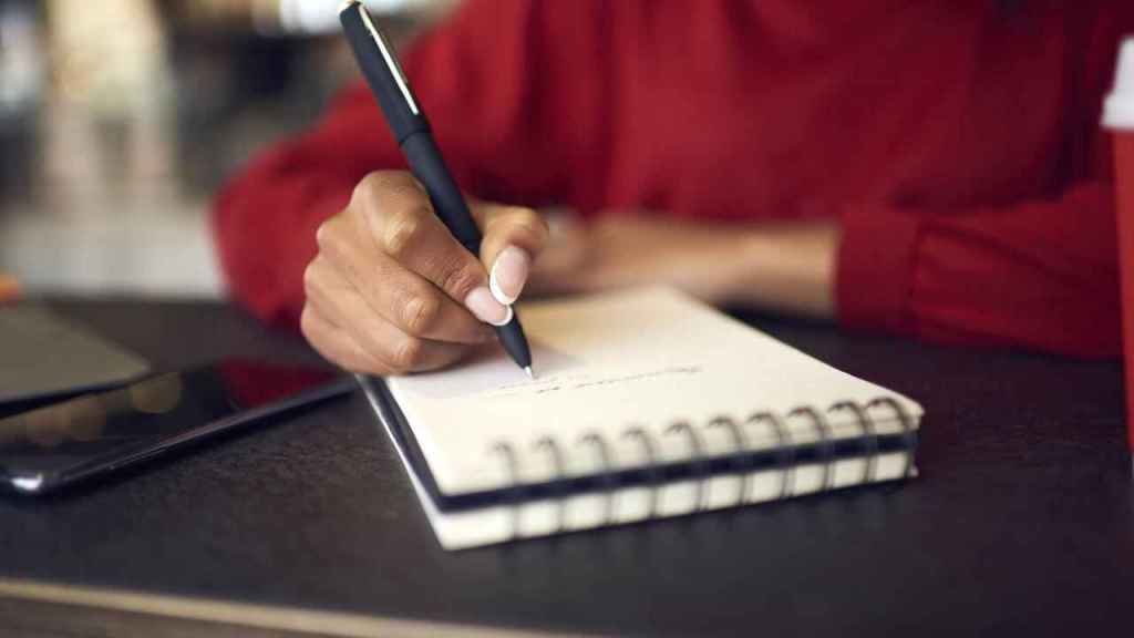 Woman at desk with notebook writing a list.